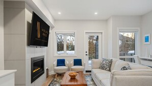 Una sala moderna con chimenea, dos sillones, un sofá, una mesa de centro y un televisor montado en la pared.