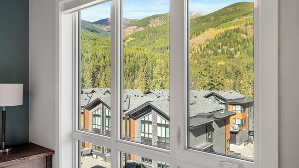 Una habitación con ventanas amplias que ofrecen vistas a un paisaje montañoso y otros edificios.