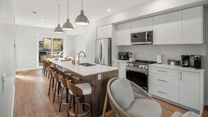 Una cocina moderna con armarios blancos, electrodomésticos de acero inoxidable y una isla central con taburetes de bar.