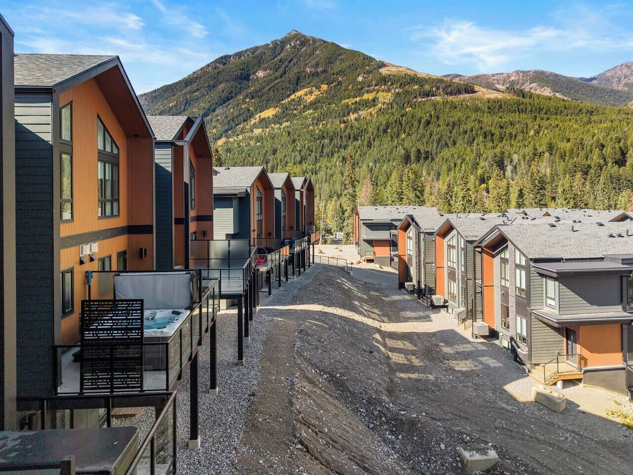 A row of modern cabins with large windows, a gravel path, and a mountainous backdrop.