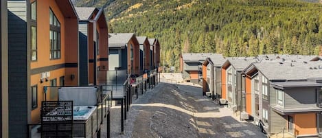 A row of modern cabins with large windows, a gravel path, and a mountainous backdrop.