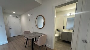Un apartamento moderno con comedor que incluye una mesa y sillas, un baño con inodoro y lavamanos, y un pasillo que conduce a otra habitación.