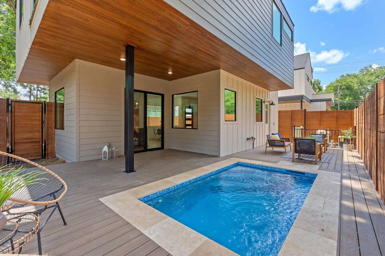 A modern house with a wooden deck, a swimming pool, and outdoor furniture.