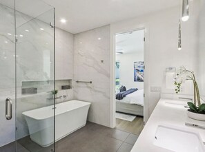 A modern bathroom with a glass-enclosed shower, a freestanding bathtub, and a white sink with a potted orchid. - Upscale Austin Getaway w/ Designer Interiors (Austin)