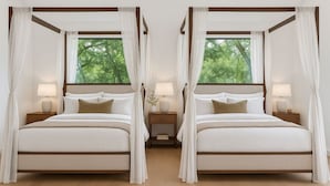 Una cama doble con dosel, mesitas de noche con lámparas y vistas a árboles por la ventana.