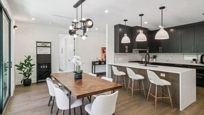 Una cocina moderna con una isla central, taburetes blancos y luces colgantes.