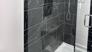A modern bathroom with a glass-enclosed shower, dark marble tiles, and a white bathtub. - Spacious Cedar Park Retreat (Cedar Park)