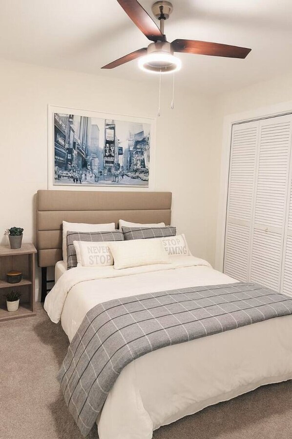 A bedroom with a bed, a ceiling fan, a nightstand, a framed cityscape picture, and a closet with louvered doors. - Modern 4BR Retreat w/ Hot Tub & Huge Backyard (Cedar Park)