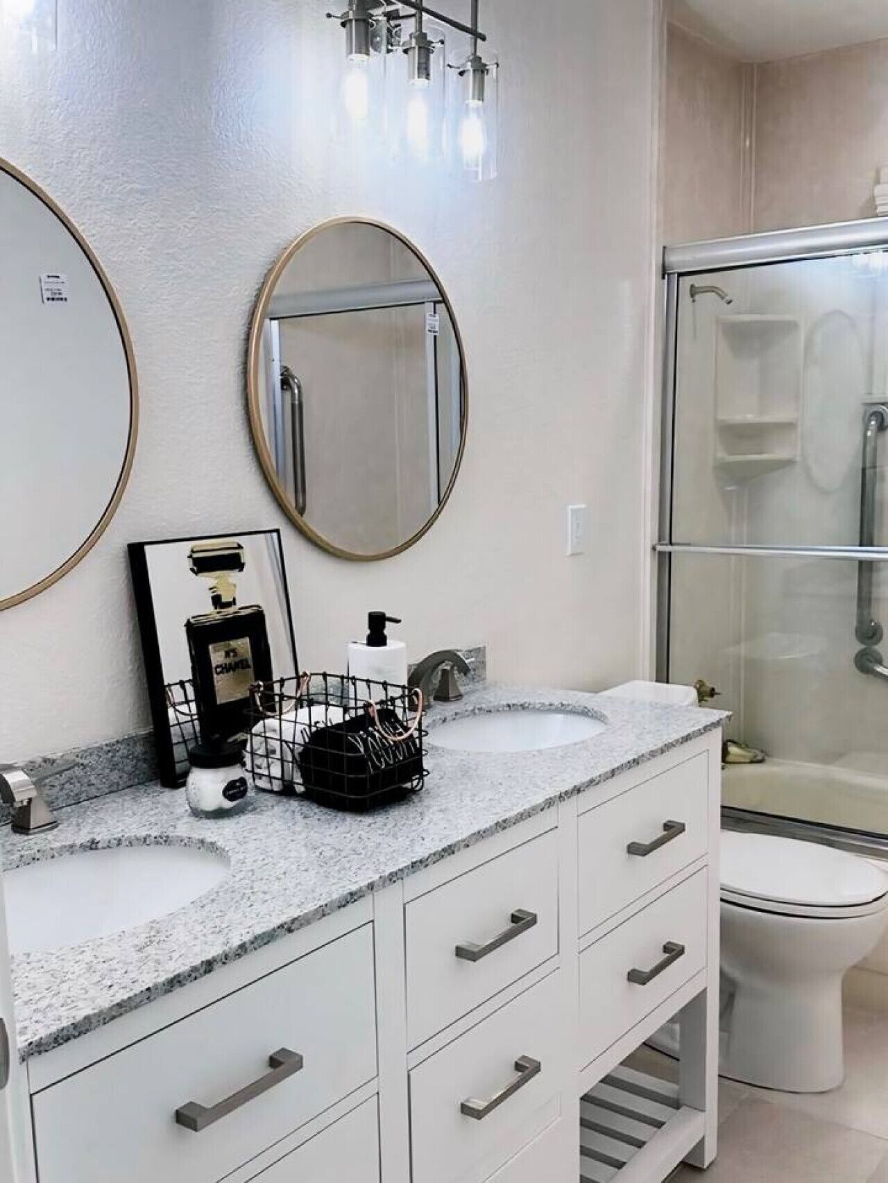 Une salle de bain moderne avec un comptoir en granit, deux grands miroirs, un lavabo blanc, une cabine de douche et des toilettes.