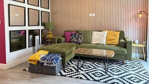 Uma sala de estar moderna com um sofá verde, um tapete estampado e um espelho fixado na parede.
