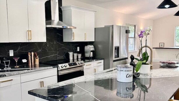 Une cuisine moderne avec des meubles blancs, un îlot central et un plan de travail noir.