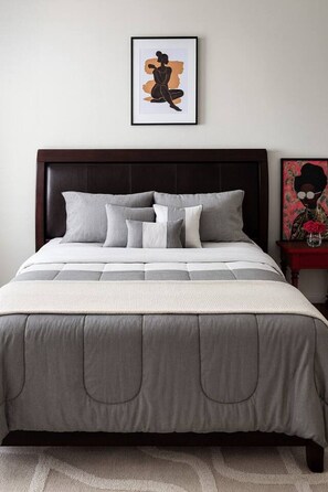 A neatly made bed with a grey and white duvet, a dark headboard, and a framed artwork above it. - Spacious Cedar Park Retreat | Backyard Oasis (Cedar Park)