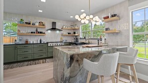 Een moderne keuken met een marmeren eiland, groene kastjes en hanglampen.