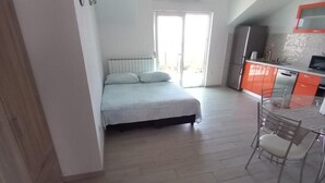 Ein Schlafzimmer mit einem Bett, einem kleinen Tisch mit Stuhl und einer Küchenzeile mit orangenen Schränken.