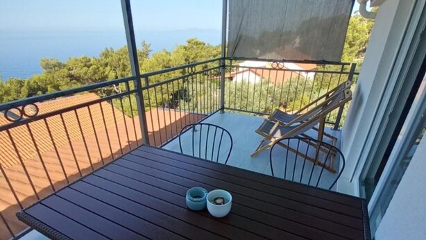 Ein Balkon mit Holztisch, zwei Stühlen und Meerblick.