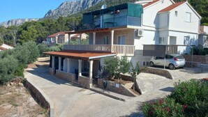 Ein zweigeschossiges Haus mit einem Balkon, einer überdachten Terrasse und einem Auto auf der Auffahrt.