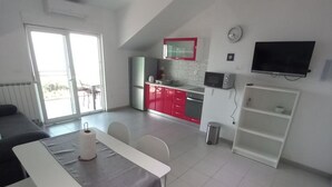 Een moderne keuken met rode kastjes, een magnetron en een televisie. Er is een eethoek met een tafel en stoelen.