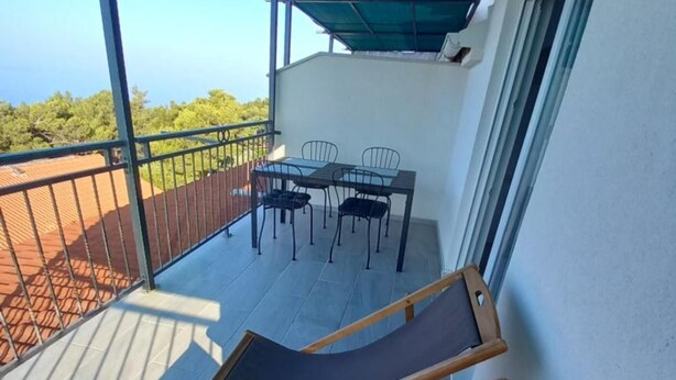 Een balkon met een tafel en stoelen, een houten stoel, en uitzicht op de omgeving.