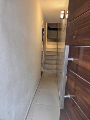 A narrow hallway with a staircase leading to an upper floor. The walls are plain, and there is a wooden door on the right. - In the historical center and with all services nearby. (Arequipa)