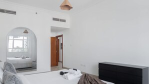 A modern hotel room with a large bed, a black dresser, and a view of the city through an arched window. - JVC 1 bed Sleeps 4 With Swimming Pool (Dubai)
