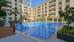 A large indoor swimming pool surrounded by a multi-story hotel building with balconies. - JVC 1 bed Sleeps 4 With Swimming Pool (Dubai)