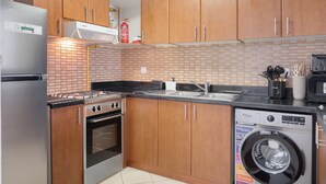A compact kitchen with wooden cabinets, a stainless steel refrigerator, a built-in oven, a gas stove, a sink, and a front-loading washing machine. - JVC 1 bed Sleeps 4 With Swimming Pool (Dubai)