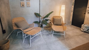 A room with two wicker chairs, a potted plant, and a wall-mounted light fixture. - Flor De India (San Juan)