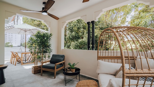 A modern outdoor seating area with wicker furniture, a ceiling fan, and a view of greenery. - Flor De India (San Juan)