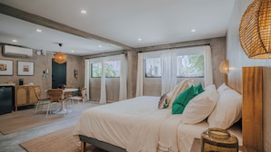 A modern bedroom with a large bed, a dining area, and a kitchenette. - Flor De India (San Juan)