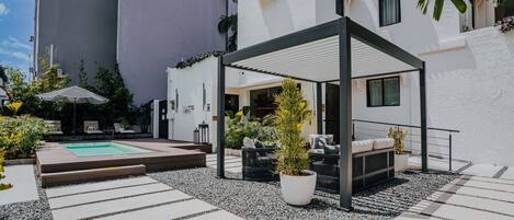 A modern outdoor patio with a pool, seating area, and potted plants.