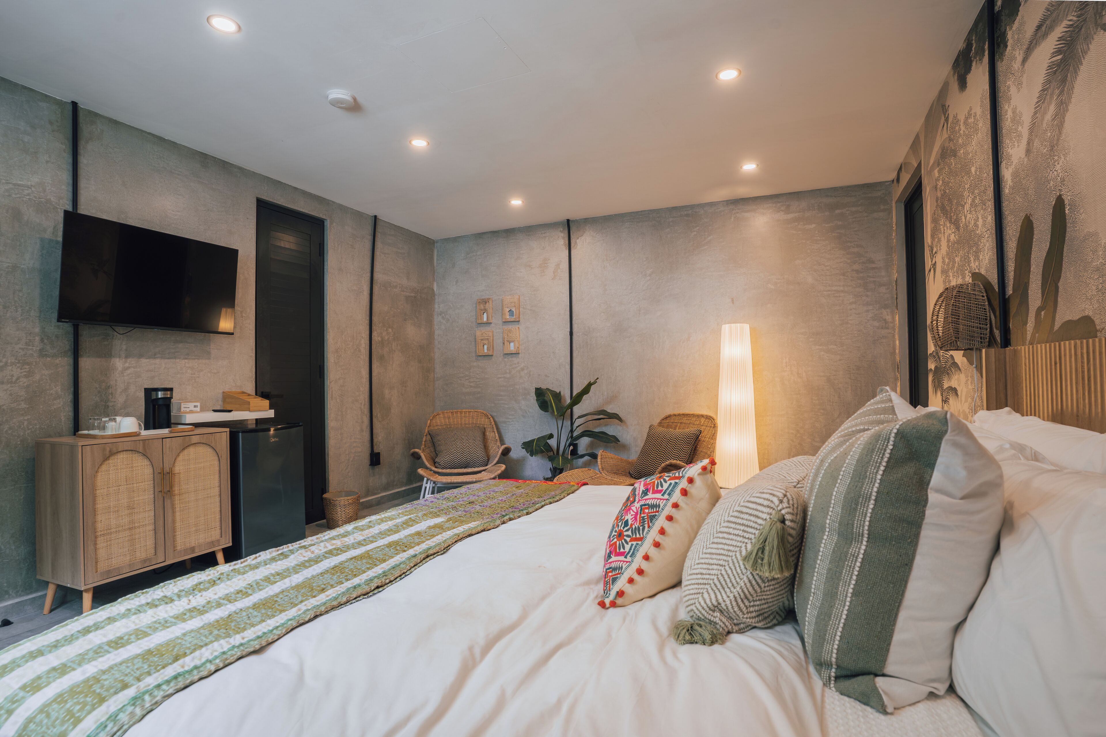 A modern hotel room with a bed, a television, a small desk, and a seating area with chairs.
