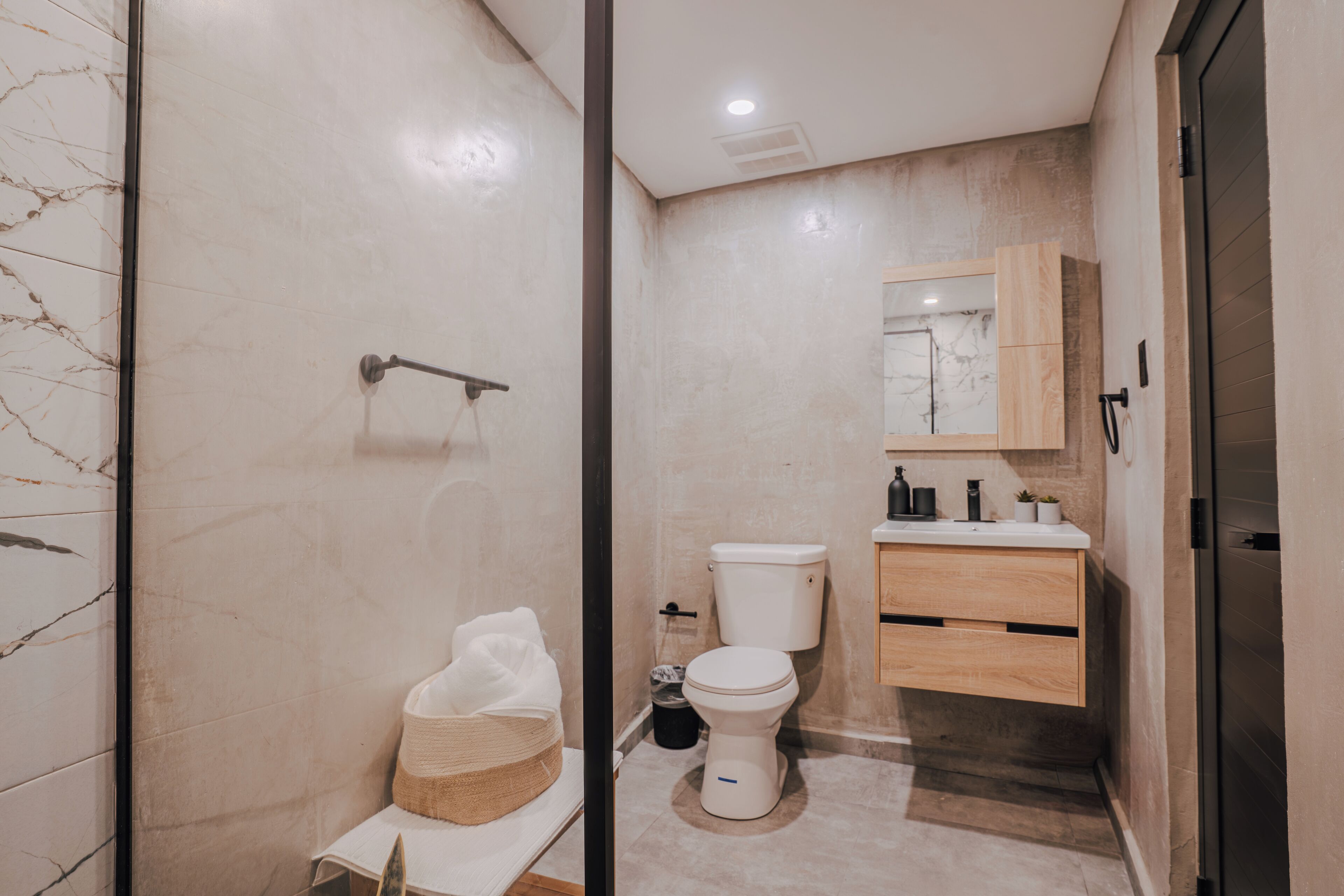 A modern bathroom with a marble wall, a toilet, a sink with a mirror, and a shower area.