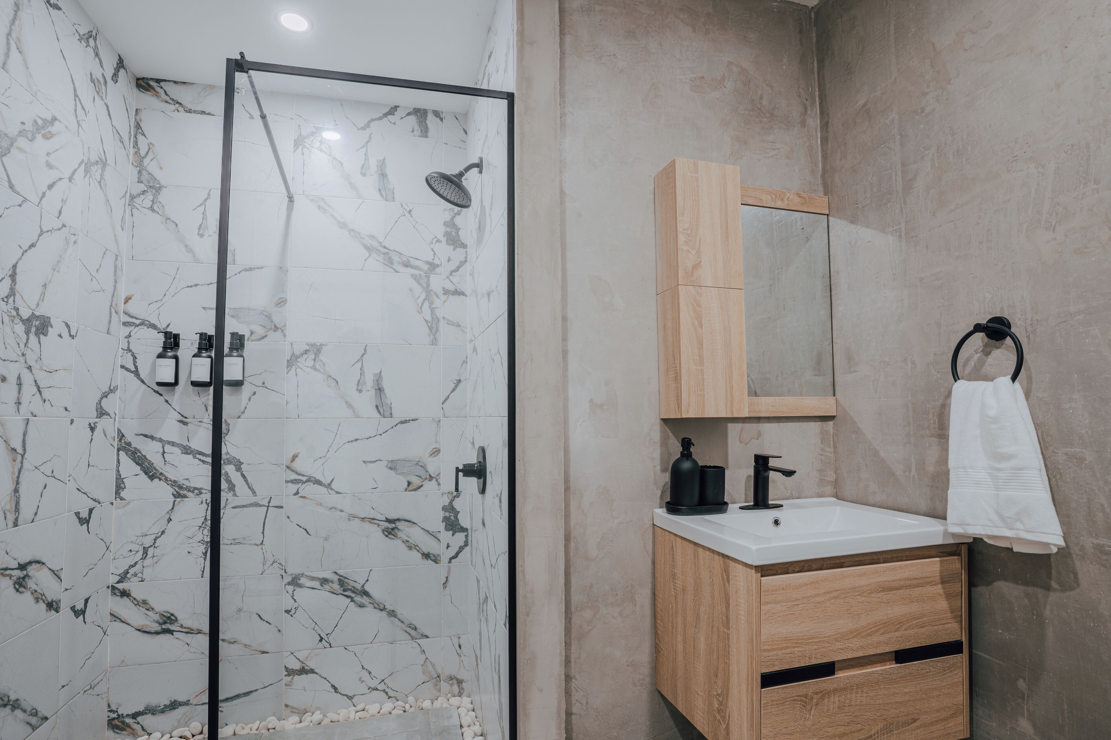 Un baño moderno con ducha de vidrio, tocador de madera con espejo y lavamanos blanco.