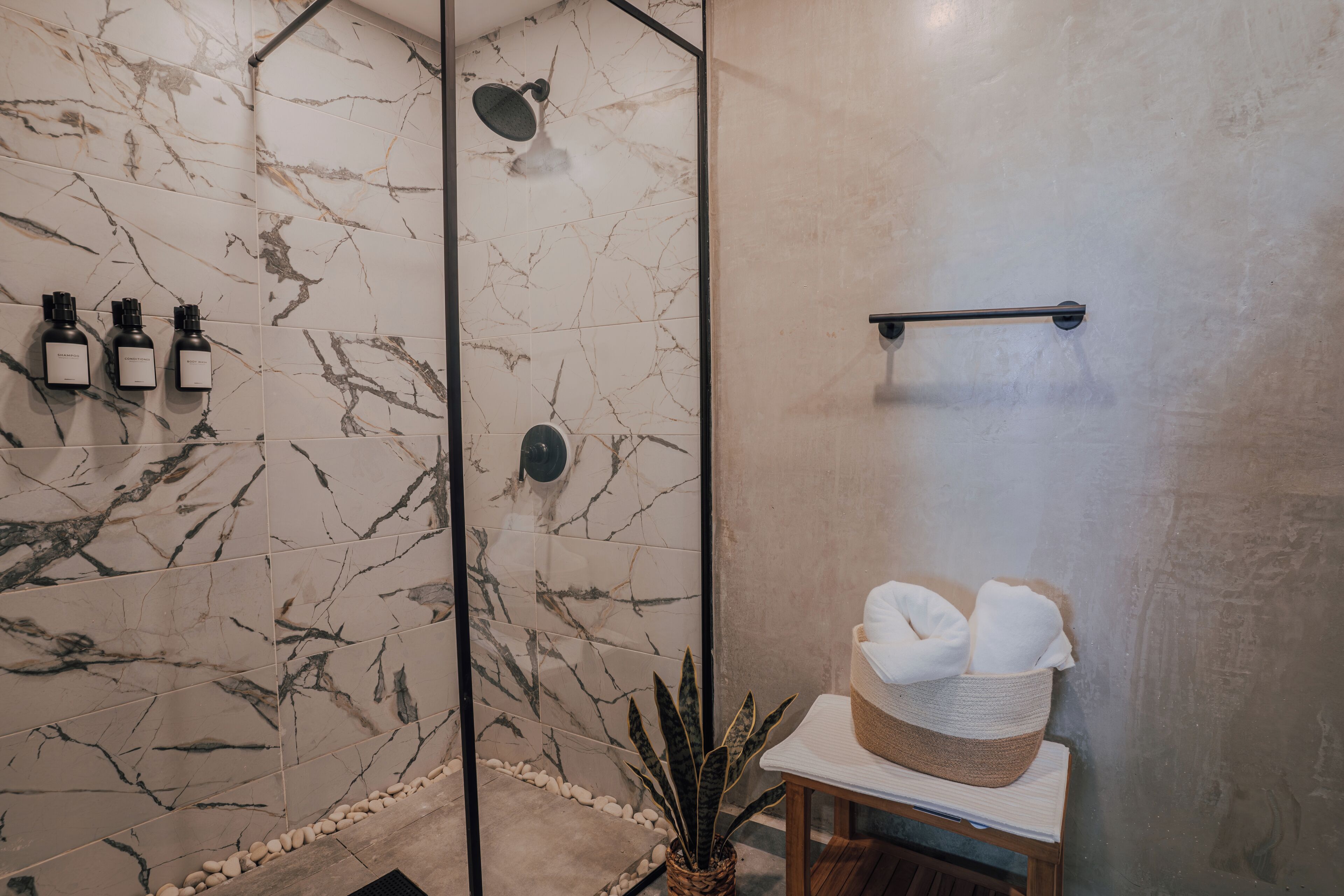 A bathroom with marble tiles, a shower, a towel rack, and a plant.