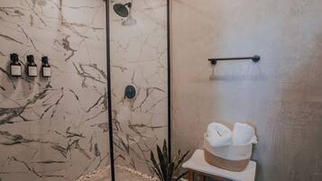 A bathroom with marble tiles, a shower, a towel rack, and a plant.