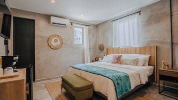 A bedroom with a bed, a bedside table, a nightstand, a window with curtains, a wall-mounted air conditioner, and a small decorative item on the nightstand.