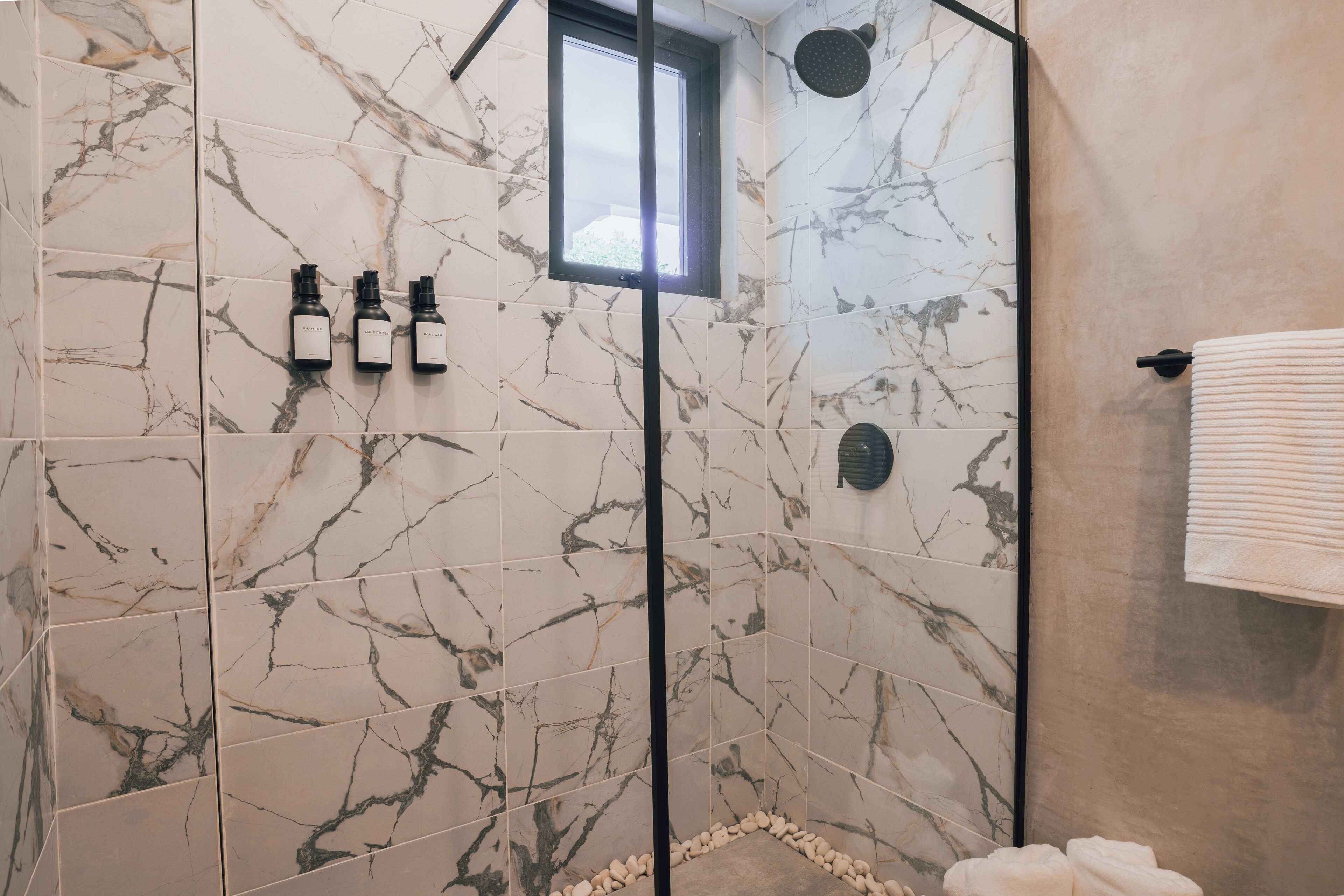 Un baño con azulejos de mármol, ducha con cerramiento de vidrio y un perchero para toallas.