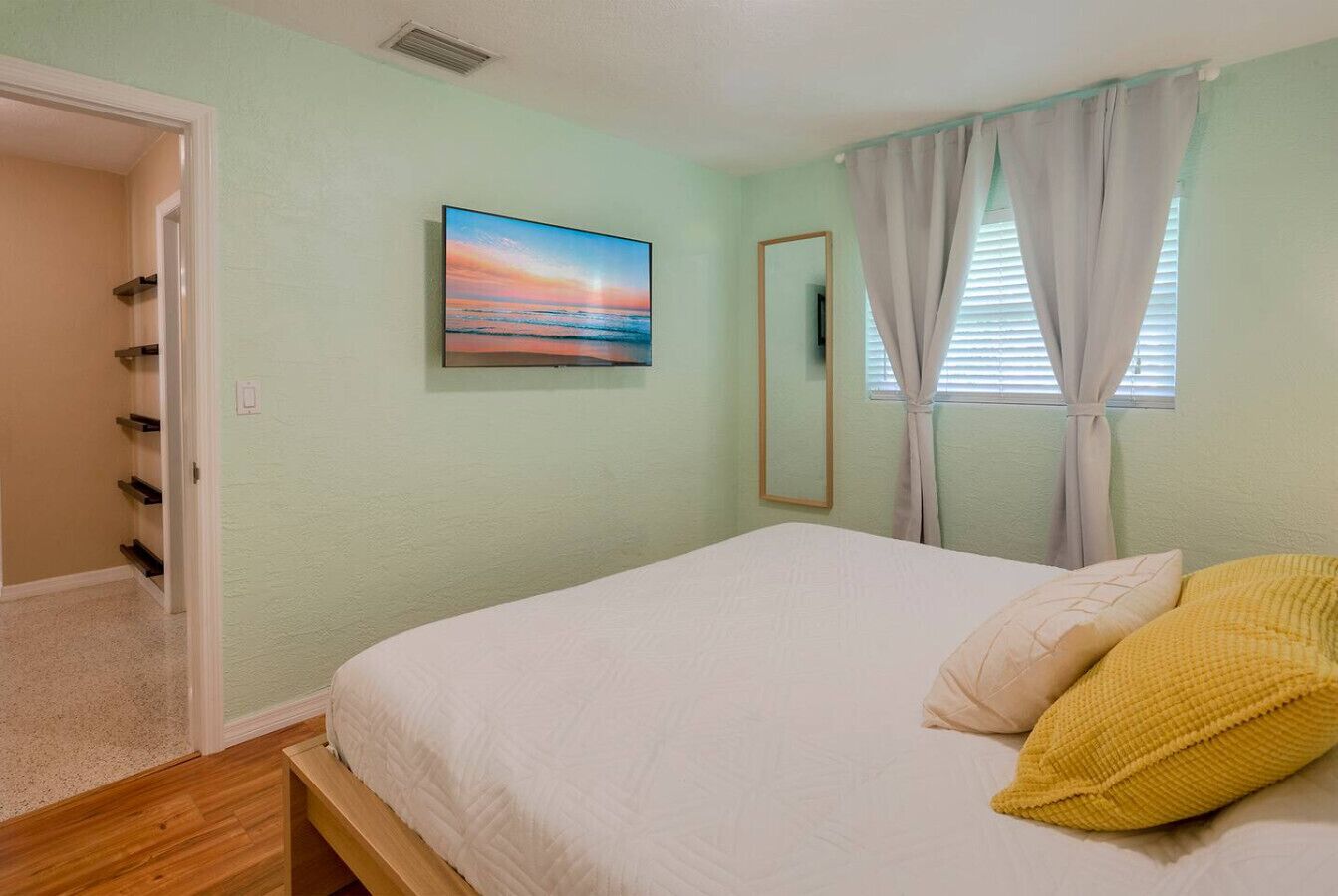 A bedroom with a bed, a painting, a window with curtains, and a door.
