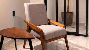 A modern chair with a cushioned seat and wooden armrests, placed on a marble floor.
