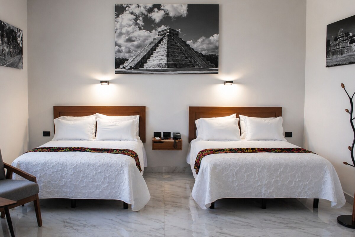 A hotel room with two beds, a chair, a nightstand, and a wall-mounted lamp.
