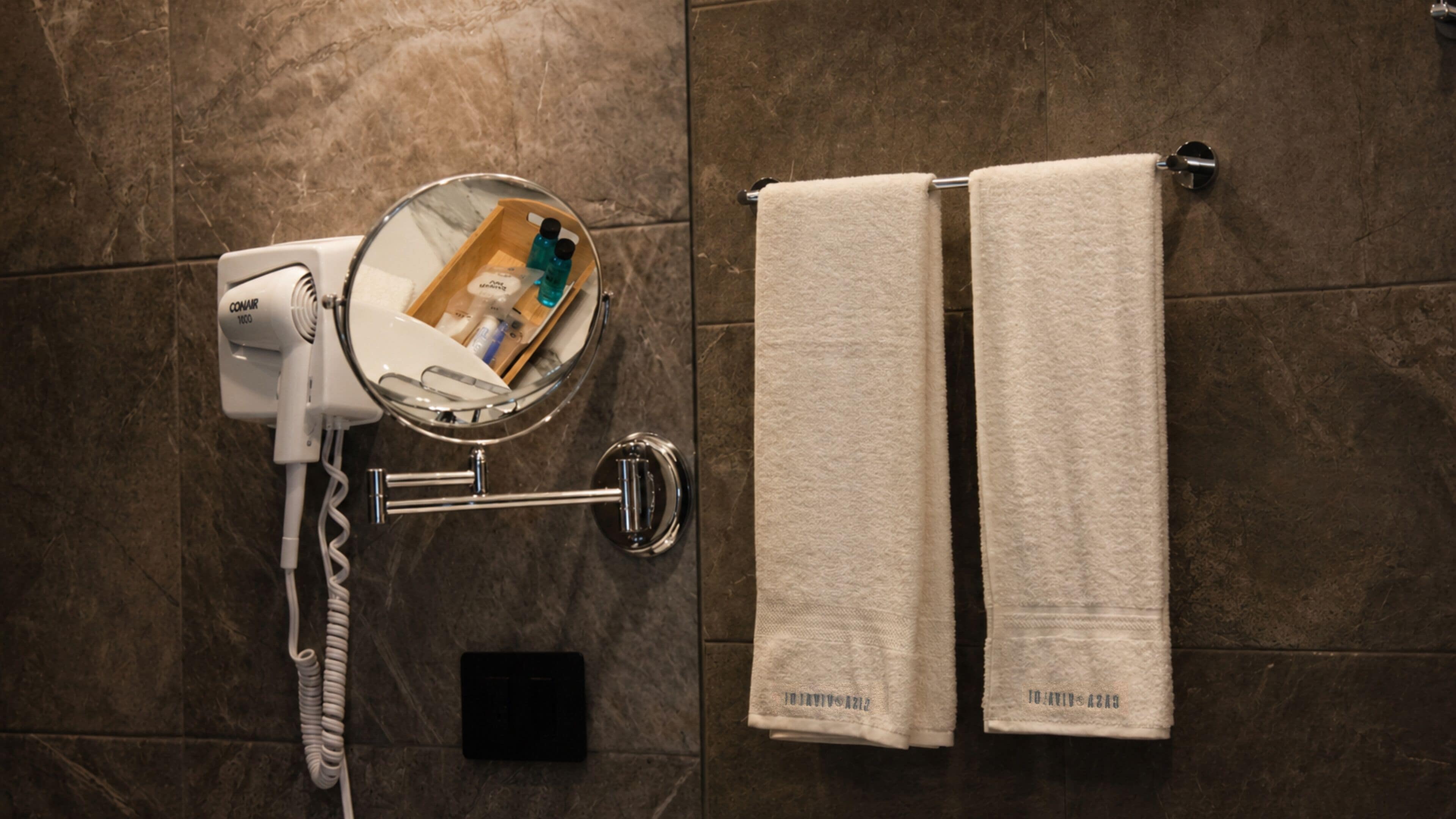 Un baño con secador de pelo, espejo y dos toallas colgadas en la pared.