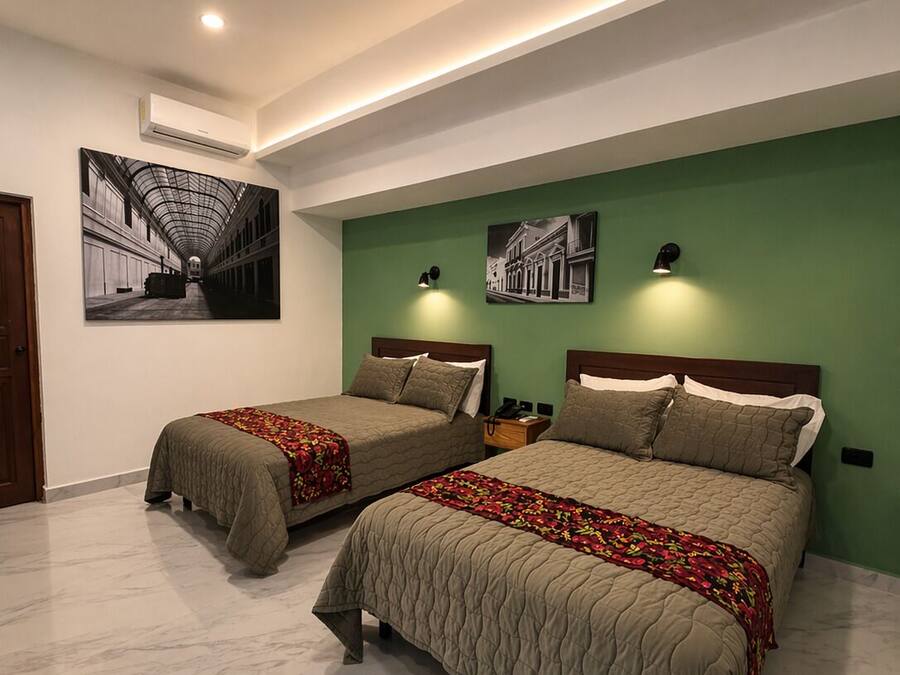 A hotel room with two beds, a ceiling fan, wall-mounted artwork, and a green accent wall.