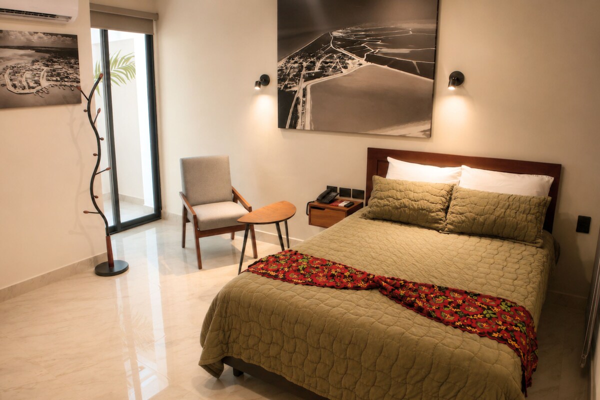 A hotel room with a bed, a chair, a nightstand, and two wall-mounted lamps.