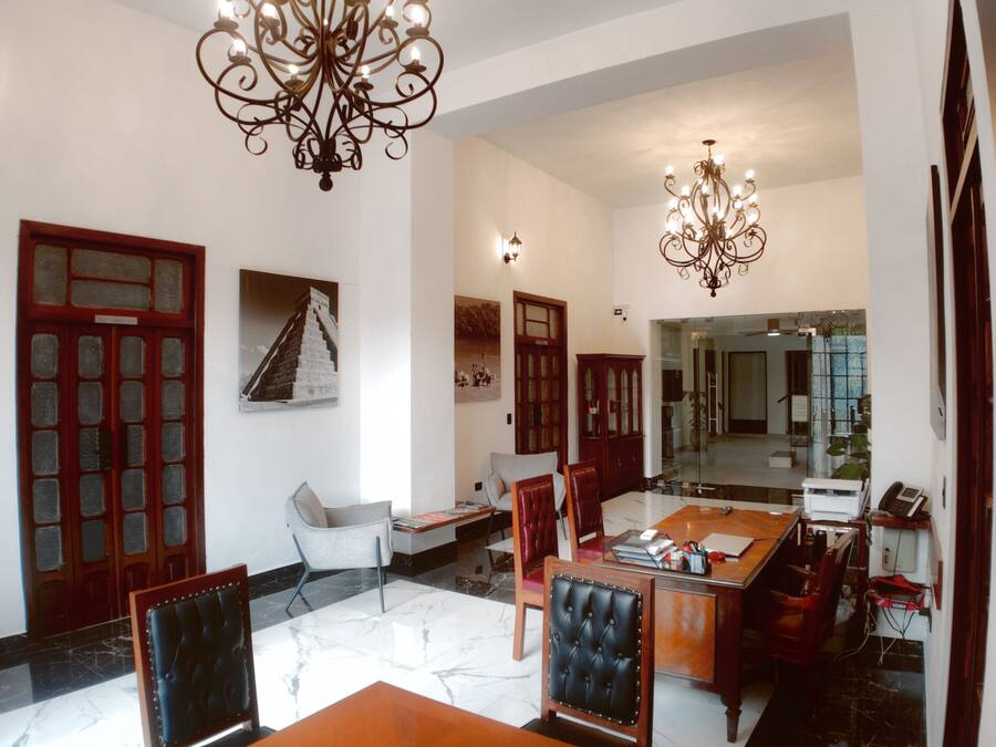 A spacious hotel lobby with a marble floor, a dining area with a wooden table and chairs, and two chandeliers.