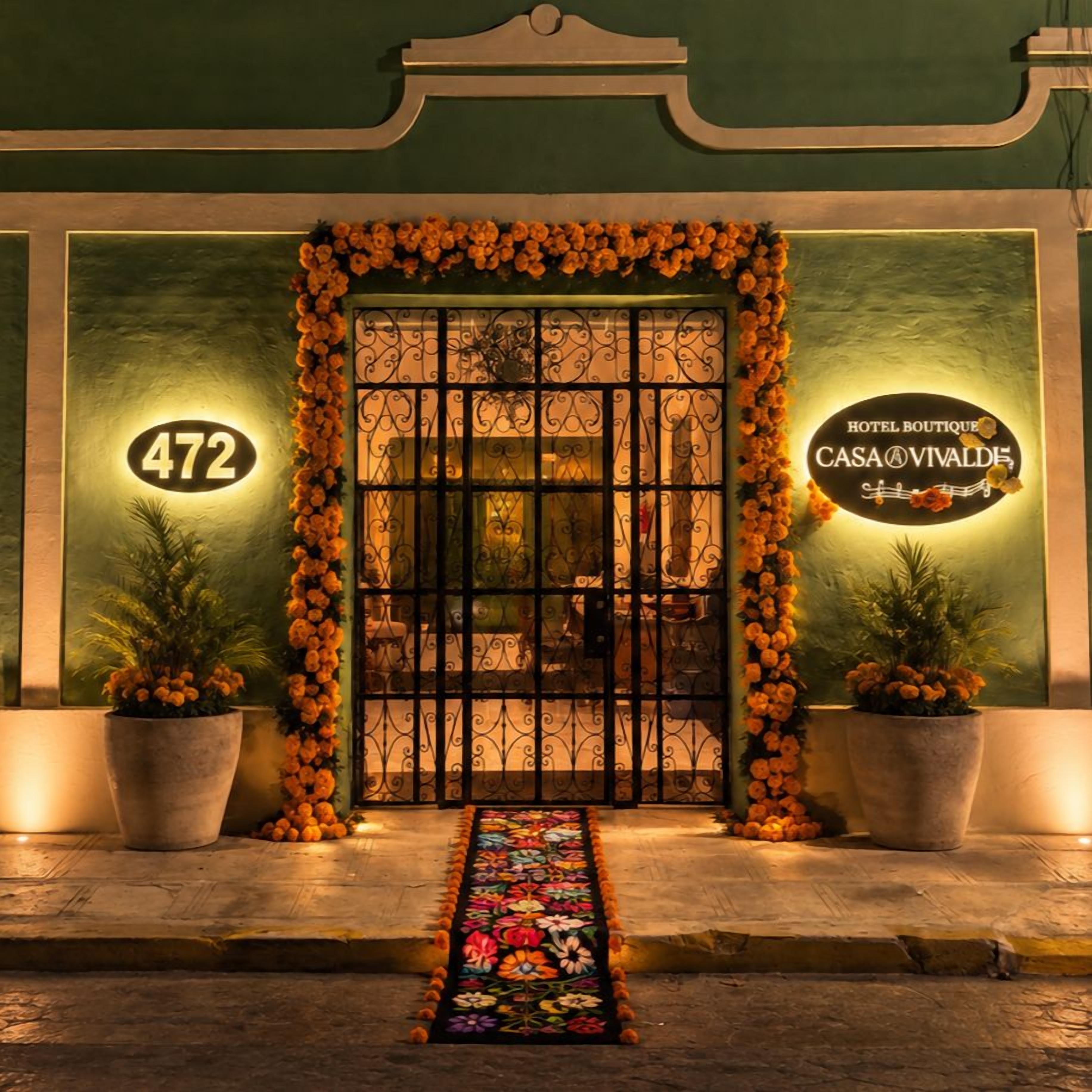 Entrada de un hotel con un letrero con el número '472', un arco floral decorativo y un cartel que dice 'HOTEL BOUTIQUE CASA VIVALDI'.