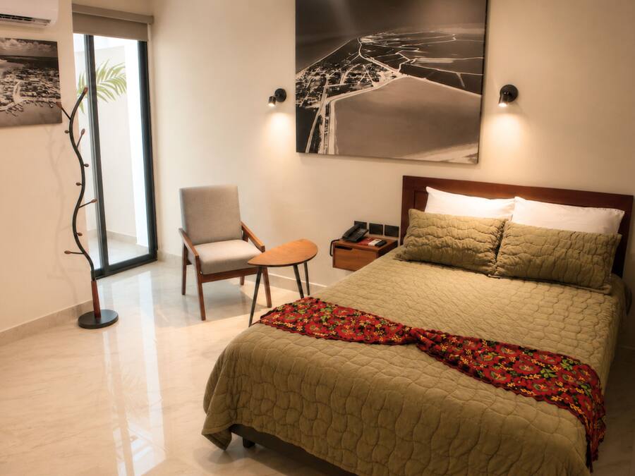 Habitación de hotel con una cama, una silla, una mesita de noche y dos lámparas fijadas a la pared.