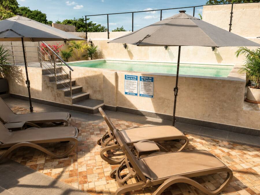 A rooftop pool area with lounge chairs, umbrellas, and a sign with pool rules.