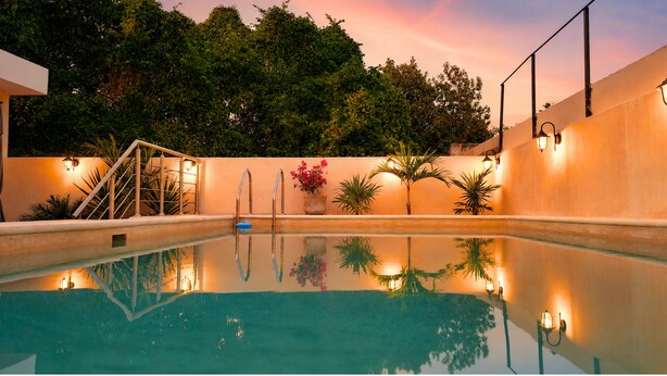 A swimming pool with a clear reflection, surrounded by a wall with potted plants and a staircase.
