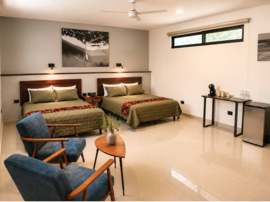A hotel room with two beds, a desk, a chair, a small table, and a plant.