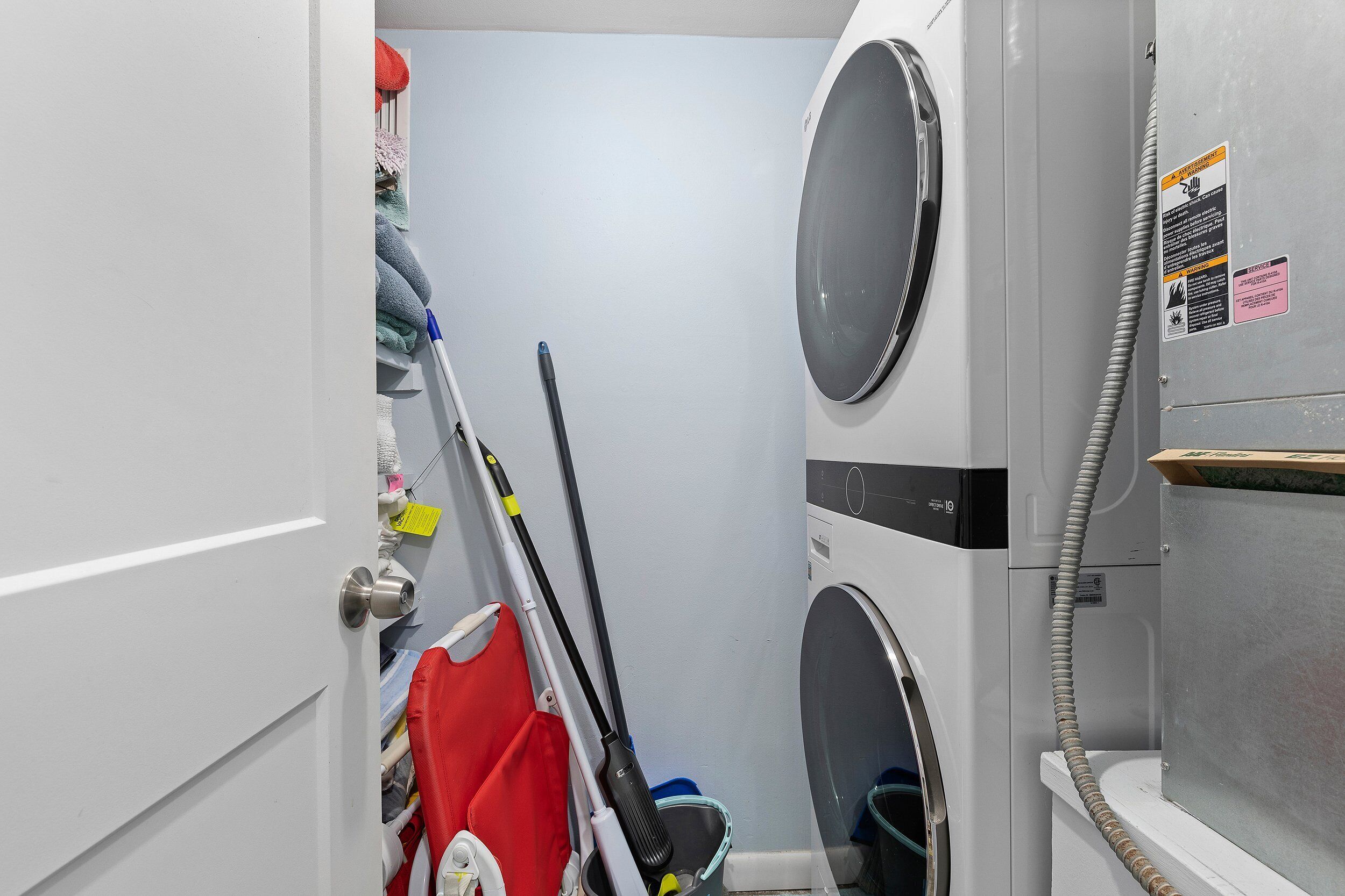 A laundry room with stacked laundry, a mop, and a broom.